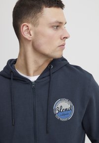 Mornarska zip-up dukserica od mješavine pamuka s jednostavnom teksturom. Sadrži okruglu zakrpu s logotipom: "Blend California, Vintage Denim."