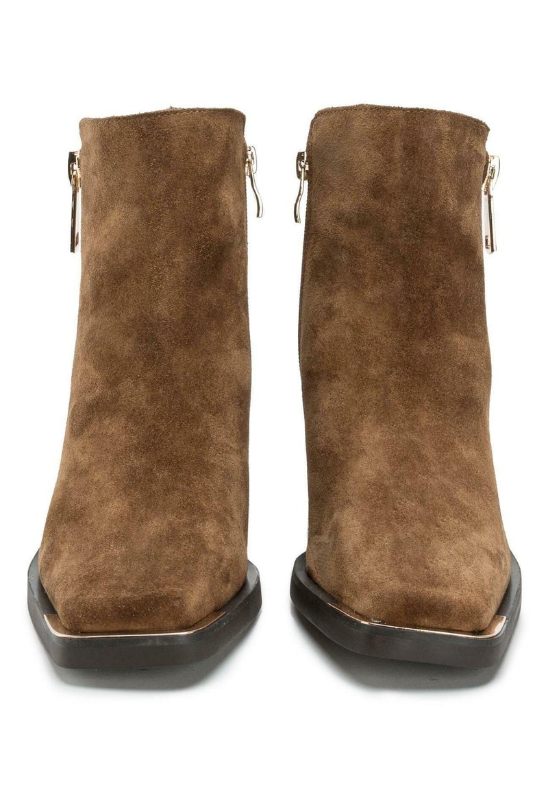 Botas de tobillo de ante marrón con punta cuadrada, cremallera plateada en el lateral y suela plana negra, con un acabado liso y texturizado.