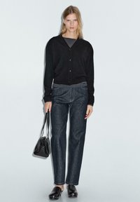 Svart cardigan, randig skjorta under, mörkblå raka jeans, svart handväska och träskor med silvernitar. Enkel och modern design.