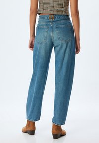 Jeans de mezclilla azul de pierna ancha con una cintura alta, cinco bolsillos y un acabado desgastado. Combinados con botas de tacón marrón claro.