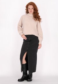 Hellbeige gestrickter Pullover mit hohem Kragen, kombiniert mit einem schwarzen Jeans-Maxikleid mit seitlichem Schlitz und schwarzen Knöchelstiefeln.