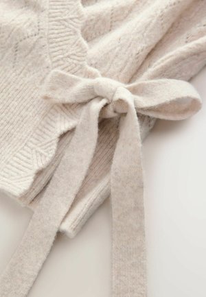 Pull en maille beige clair avec des motifs texturés, des bords côtes et un nœud attaché sur le côté. Matière douce et confortable.