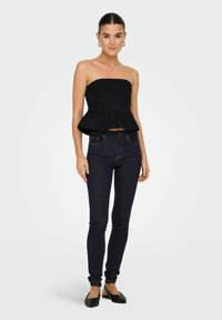 Top peplum negro sin mangas con un corsé ajustado, combinado con jeans oscuros ajustados y planos negros. Tejido suave con un brillo sutil.