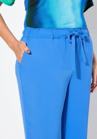 Pantalones azul claro hechos de tela suave, con una cinturilla elástica con un lazo y bolsillos laterales. Textura suave y ajuste relajado.