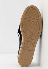 Semelle d'une espadrille noire avec un dessous en caoutchouc texturé couleur tan, taille 37, présentée debout verticalement sur un fond blanc.
