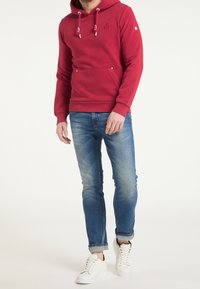 Czerwona bluza z kapturem, białymi sznurkami, kieszenią kangurką oraz logo. Zestawiona z niebieskimi obcisłymi dżinsami i białymi trampkami.
