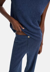 Granatowy, strukturalny zestaw topu i spodni, charakteryzujący się luźnym krojem, poziomymi prążkami oraz ozdobnym złotym guzikiem na pasku.