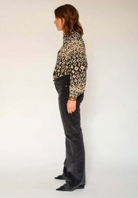 Blouse noire imprimée avec des motifs géométriques, associée à un jean en velours côtelé foncé évasé. Les accessoires comprennent un bracelet et des chaussures noires à bout pointu.