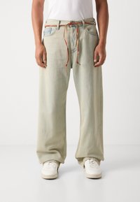 Light blue wide-leg jeans made of denim, featuring a drawstring waist with red and brown accents. Paired with white sneakers.