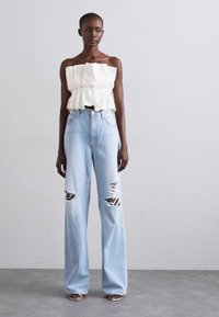 Vit, rufsig strapless topp i kombination med ljusblå, högmidjade jeans med rippade detaljer och sandaler med remmar. Slätt tyg, lös passform, avslappnad stil.
