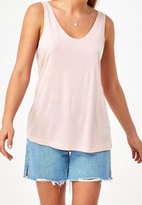 Top senza maniche di un rosa chiaro con scollatura a V, realizzato in un materiale morbido e liscio, abbinato a pantaloni di jeans strappati con fessure laterali.