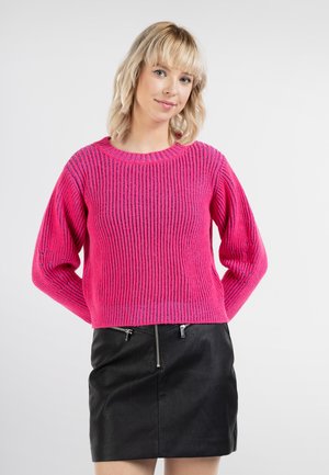 Pulover roz tricotat cu o textură în caneluri, guler rotund și mâneci largi, asortat cu o fustă din piele neagră cu detalii cu fermoar.