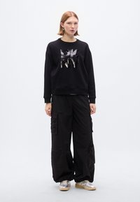 Μαύρο φούτερ με το γράφημα "DKNY", σε συνδυασμό με φαρδιά μαύρη παντελόνια cargo με τσέπες και φερμουάρ. Ασημένια αθλητικά παπούτσια ολοκληρώνουν το σύνολο.