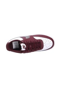 Les baskets Nike présentent un dessus en cuir maroon avec des panneaux perforés blancs, des accents gris et un design de lacets texturé en maroon.