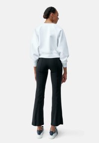 Sweatshirt blanc avec des manches bouffantes et un ourlet côtelé, associé à un pantalon noir évasé avec des coutures latérales et un design ajusté.