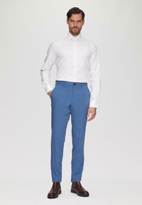 Blaue maßgeschneiderte Hosen mit glatter Textur, kombiniert mit einem weißen Hemd mit Knöpfen. Die Hosen haben ein elegantes Design und Fronttaschen.