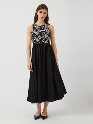 Svart ermeløs kjole med brodert kropp og blomsterdesign, teksturert stoff og en utsvingt skjørt som går til midtleggen.