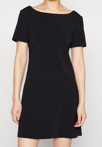 Vestido negro de manga corta con un escote amplio, textura suave y un corte relajado. El diseño presenta una silueta recta y un dobladillo a la altura de la rodilla.
