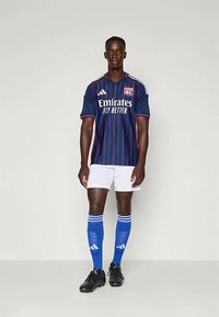 Sininen jalkapallopaita valkoisilla yksityiskohdilla, jossa on vaaleita vaakaraitoja ja logoja. Valkoiset shortsit, siniset sukat valkoisilla raidoilla ja mustat nappulakengät.