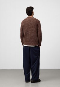 Brązowy sweter z dzianiny o okrągłym dekolcie, zestawiony z luźnymi granatowymi spodniami. Sweter ma teksturowane, puszyste wykończenie.