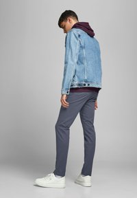 Chaqueta de mezclilla azul claro sobre una sudadera burdeos, pantalones grises y zapatillas blancas. La chaqueta tiene un acabado desgastado con costuras visibles.