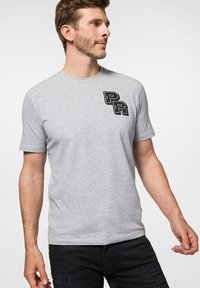 Szara bawełniana koszulka z krótkim rękawem i okrągłym dekoltem, z czarnym logo "PR" wydrukowanym po lewej stronie klatki piersiowej.