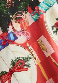 Festive table setting with a red checkered tablecloth, a glass, white plates, golden cutlery, and gifts wrapped in shiny ribbons.