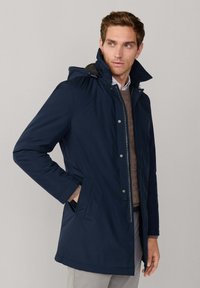 Marineblauer Parka mit Reißverschluss und Druckknopfverschluss, Kapuze, seitlichen Taschen und weicher Innenauskleidung, mit lässiger Passform und glatter Textur.