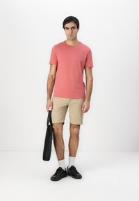 Pink short-sleeved t-shirt, beige shorts, black sneakers, holding a black bag. Simple design, crew neck, relaxed fit, and a smooth texture.
