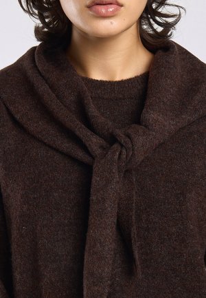 Vrouw draagt een donkerbruine gebreide trui met een bijpassende sjaal los gestrikt rond haar nek.