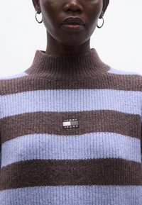 Kötött pulóver barna és világoskék vízszintes csíkokkal. Magas nyakú kialakítás texturált anyagból, "TOMMY JEANS" logóval.
