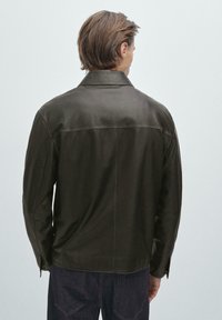 Mörkbrun läderjacka med krage, slät textur och synliga sömnadsdetaljer. Långa ärmar med knäppningar vid handledarna.