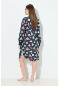 Camicetta da notte blu navy con una stampa diornamenti festivi in rosso, verde e bianco. Maniche lunghe, colletto a bottoni e fessure laterali per facilitare i movimenti.