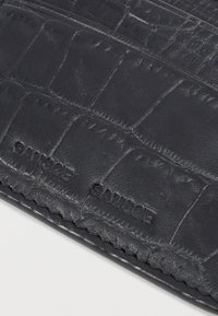 Nahaufnahme einer schwarzen Lederbrieftasche mit Krokodilstruktur und eingeprägtem Markennamen "SAMSOE SAMSOE" auf der Oberfläche.