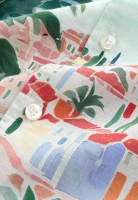 Tissu léger avec des maisons abstraites colorées et des motifs de feuillage, comportant des boutons blancs et des coutures visibles.