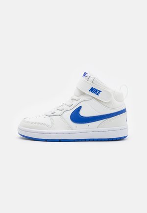 Baskets montantes Nike blanches et bleues avec logo swoosh bleu, fermeture à lacets et bride Velcro sur fond gris clair uni.