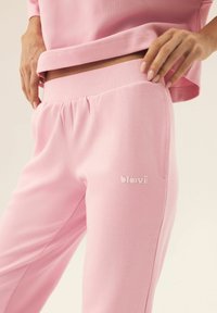 Różowe spodnie dresowe z miękkiego materiału z elastycznym paskiem. Posiadają boczną kieszeń oraz małe, wytłoczone logo na udzie.