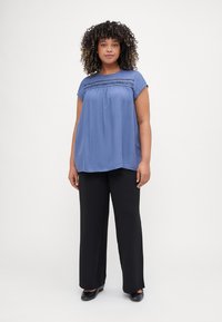 Loose-fitting blue blouse with short sleeves, featuring decorative stitching across the chest, paired with black wide-leg trousers.