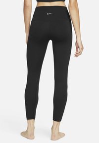 Czarne legginsy sportowe z wysokim stanem, wykonane z elastycznego materiału, z małym srebrnym logo Nike z tyłu i płaskimi szwami.