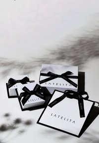 Három téglalap alakú ajándékdoboz fehér színben, fekete díszítésekkel és szalagokkal, mindegyiken a "LATELITA" logóval a doboz felületén.