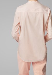 Chemise à manches longues rose clair avec des rayures verticales, ourlet arrondi, empiècement au dos et détails de manches à boutons. Fabriquée dans un tissu doux et texturé.