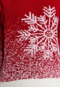 Punainen neulepaita, jossa on valkoinen lumihiutale-kuvio, ja hemman alaosa on ombre-efektillä, joka siirtyy punaisesta valkoiseen. Pehmeä rakenne.