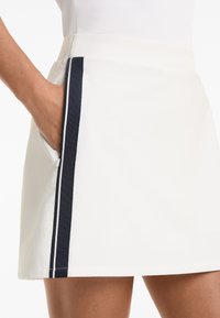 White skirt featuring a navy side stripe, made from smooth fabric with a zip pocket detail. Designed for a fitted silhouette.