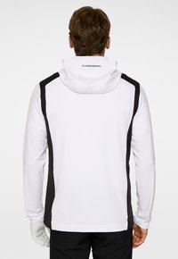 Vit hoodie med svarta sidodetaljer, justerbar huva och logotypdetalj på baksidan. Har en mjuk textur och atletisk passform.