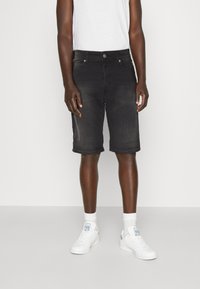 Shorts din denim negri cu croială slim, design cu cinci buzunare și manșete pliate, purtați cu adidași albi și șosete până la glezne.
