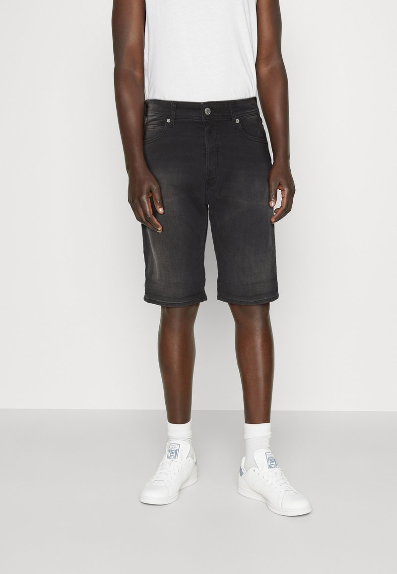 Shorts din denim negri cu croială slim, design cu cinci buzunare și manșete pliate, purtați cu adidași albi și șosete până la glezne.