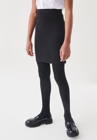 Gonna nera aderente con una texture liscia, vita alta; abbinata a collant neri opachi e mocassini neri massicci.