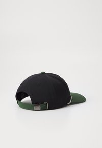 Black cap with a green brim, featuring a fabric strap at the back and a metal adjuster. Smooth textured materials throughout.