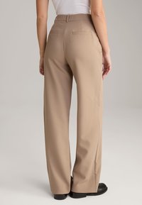 Beige weite Hosen mit glatter Textur, hoher Taille und zwei Gesäßtaschen, kombiniert mit schwarzen Schuhen.