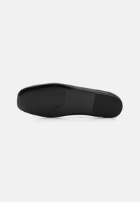 Suola di scarpa nera con una texture liscia, forma leggermente arrotondata, logo stampato lungo il lato e una base robusta e antiscivolo.